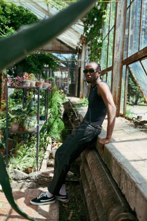 African American man in dapper style sitting on ledge in vibrant greenhouse