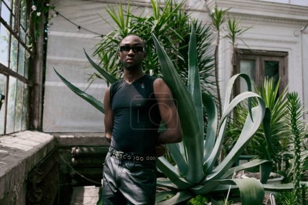 Téléchargez les photos : Homme élégant avec style dapper debout à côté d'une plante luxuriante en face d'une maison. - en image libre de droit