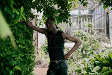 Ein gutaussehender afroamerikanischer Mann mit raffiniertem Stil steht neben einem üppig grünen Wald.