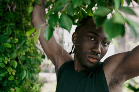Schöner afroamerikanischer Mann mit Dreadlocks, der anmutig unter einem üppigen Baum in einem lebhaften grünen Garten steht.
