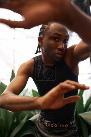 Téléchargez les photos : Un homme afro-américain élégant en chemise noire dans un jardin vert animé. - en image libre de droit