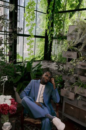 An African American man in a blue suit sits gracefully in a chair within a vibrant green garden.