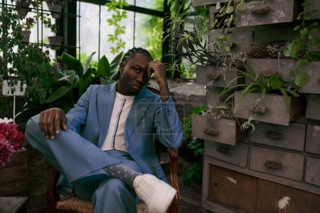 A handsome African American man in a blue suit sitting in a chair in a vivid green garden.