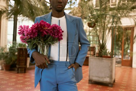 Téléchargez les photos : Un bel homme en costume tenant un bouquet de fleurs dans un jardin vert animé. - en image libre de droit