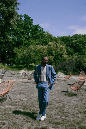 Handsome African American man in blue suit standing in lush green place.