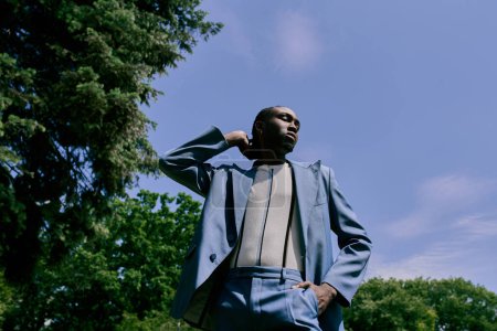Téléchargez les photos : Un homme afro-américain sophistiqué en costume et cravate se tient élégamment parmi les arbres verts vibrants. - en image libre de droit