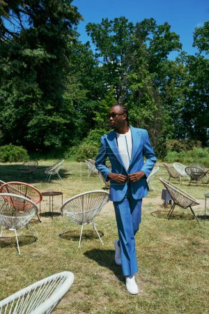 Handsome African American man in sophisticated blue suit poses in vibrant green place.