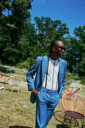 A handsome African American man in a blue suit exuding sophistication in a vibrant green place.