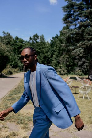 Stylish African American man in blue suit walks confidently along sidewalk.