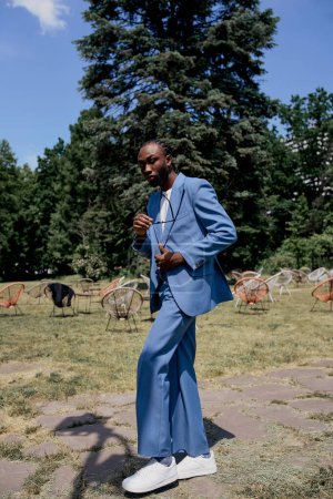 Un hombre afroamericano sofisticado con un elegante traje azul posa en un campo verde vibrante.