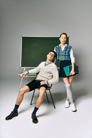 A stylish male and female student posing in front of a chalkboard at college.