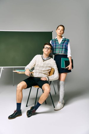 Un hombre y una mujer con estilo de pie frente a un tablero verde en la universidad.