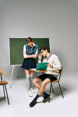 A man and a woman sit in front of a green board at college.