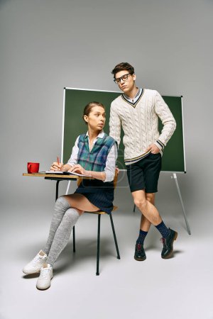 Photo for Stylish man and woman posing in front of green chalkboard in college. - Royalty Free Image