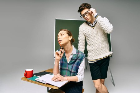 Ein Mann und eine Frau stehen elegant vor einem grünen Brett und posieren für ein College-Setting.