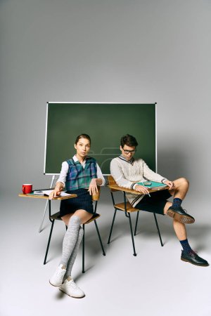 Joven hombre y mujer sentados elegantemente delante de un tablero verde en un ambiente universitario.