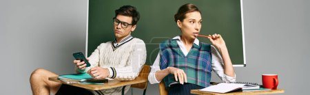 Téléchargez les photos : Deux étudiants, un homme et une femme, assis à un bureau devant un tableau noir dans un cadre universitaire. - en image libre de droit