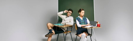 Foto de Dos estudiantes, un hombre y una mujer, se sientan en un escritorio frente a un tablero verde en un aula universitaria. - Imagen libre de derechos