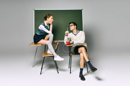 Foto de Un hombre y una mujer con estilo se sientan frente a un tablero verde en la universidad. - Imagen libre de derechos
