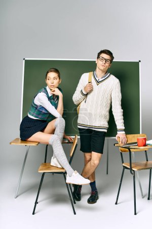 A stylish man and woman posing in front of a green board in a college setting.