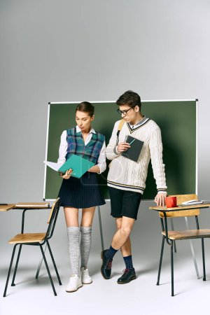 Ein stilvoller Mann und eine stilvolle Frau stehen vor einem grünen Brett in einem College-Setting.