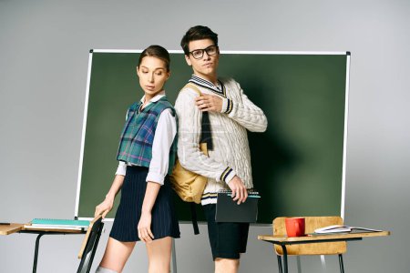 Photo for Young man and woman strike a pose in front of green chalkboard at college. - Royalty Free Image