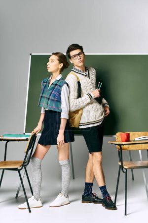 Photo for A handsome man and a beautiful woman standing confidently in front of a green chalkboard. - Royalty Free Image