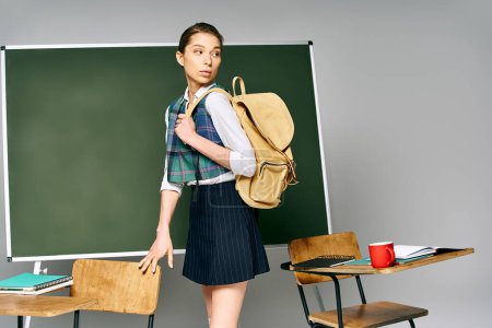 Foto de Uniformed woman with backpack stands by green board in college. - Imagen libre de derechos