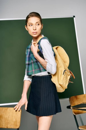 Estudiante en falda y mochila delante de pizarra.