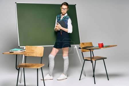 A female student in a school uniform stands before a green board.