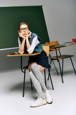 Jeune femme en uniforme assise à un bureau devant un tableau vert dans une salle de classe du collège.