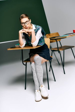 A female student in uniform sits at a desk, pondering in front of a chalkboard.