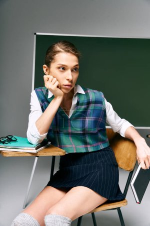 woman in uniform sits at desk in front of green board.