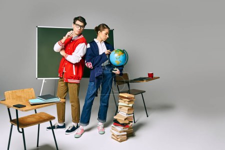Two students standing at a desk, surrounded by books and a globe.