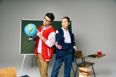 Zwei Schüler halten einen Globus in der Hand und stehen vor einem Schreibtisch in einem Klassenzimmer.