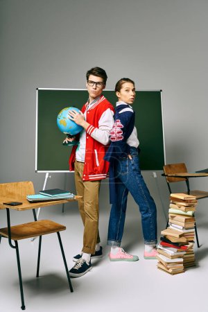 A male and female students standing by a green board with a globe in a college classroom.