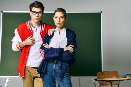 A male and female students in casual attire stand confidently in front of a green board.