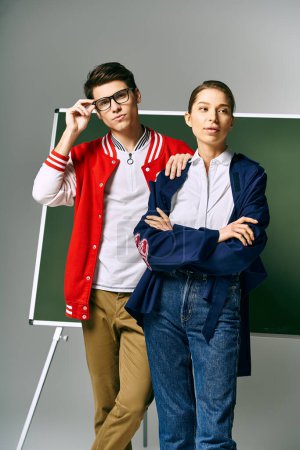 A male and female students stand in front of a green board in a college classroom.