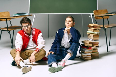 Foto de Un joven estudiante y alumna sentados en el suelo rodeados de libros en un ambiente acogedor. - Imagen libre de derechos