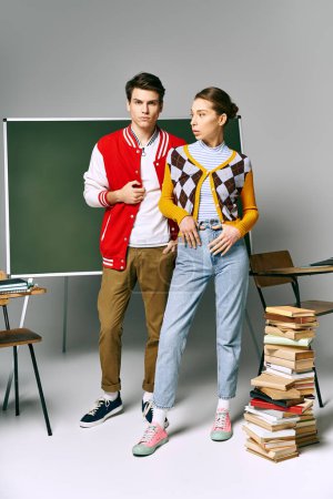 A male and female students pose elegantly in front of a stack of books.