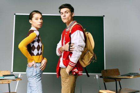 A male and female students in casual clothing stand confidently in front of a green board in a classroom.