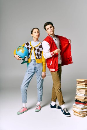 Dos estudiantes, hombres y mujeres, se paran junto a una pila de libros en un aula universitaria, posando casualmente.