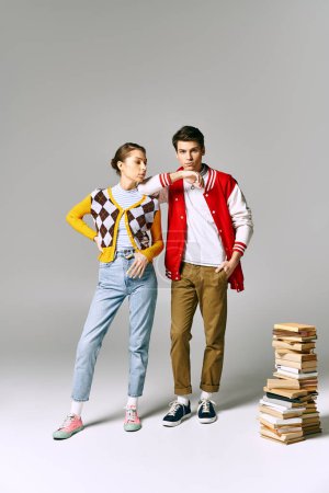 Young male and female students embracing while posing next to stack of books in college classroom.