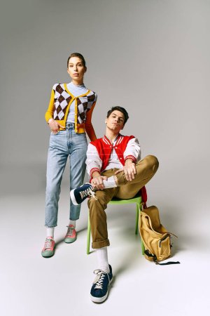 A male and female students stylishly pose on a vintage chair in a college classroom.
