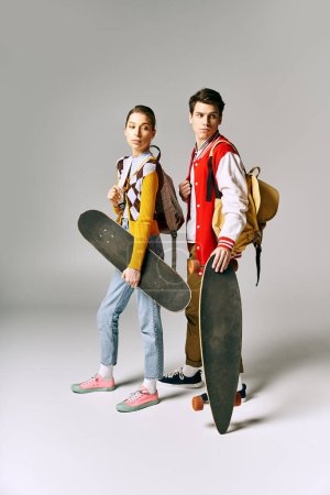 Two young people hold skateboards against a white backdrop.