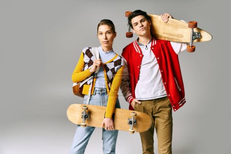 Two young people hold skateboards against a gray backdrop.