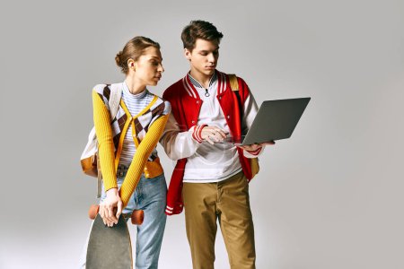 Les jeunes étudiants hommes et femmes se tiennent ensemble, tenant un ordinateur portable dans une salle de classe du collège.