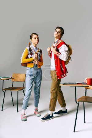 Téléchargez les photos : Deux étudiants branchés, hommes et femmes, posent près d'un bureau dans une salle de classe du collège. - en image libre de droit