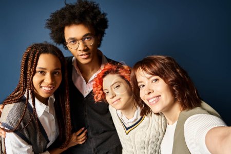 Foto de Jóvenes amigos multiculturales, incluyendo una persona no binaria, se unen con un atuendo elegante, posando para una imagen sobre un fondo azul oscuro. - Imagen libre de derechos