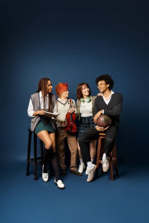 Un grupo de jóvenes amigos multiculturales, incluyendo una persona no binaria, sentados uno al lado del otro con un atuendo elegante sobre un fondo azul oscuro.